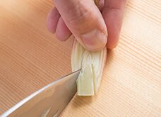 みょうがをもつ指で押さえながら、軸部分を包丁の切っ先で三角に切り落とす。