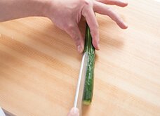 親指と人差し指できゅうりをつまむようにして押さえ、包丁の切っ先で縦半分に切る。