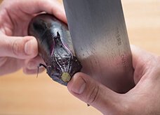 【ガクの取り方】ガクとヘタの境目に包丁の刃元をあて、ナスを持つ手で回しながらクルリとガクに切り込みを入れる。