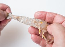 腹を上にして尾をつかみ固定する。もう片方の指で脚を尾からこそぐように取り除く。尾から1節分は残し、他の殻を全てむく。