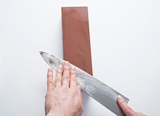 研ぐ部分の面が研ぎ石に当たるように包丁を持つ手を少し持ち上げ、包丁にわずかな角度をつけて、斜め上下に滑らせる。